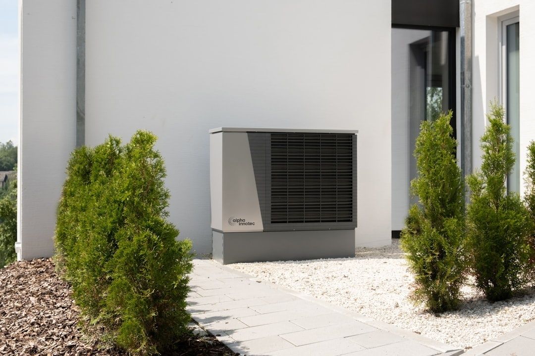 Außengerät einer Wärmepumpe vor einem modernen Wohnhaus mit Sträuchern